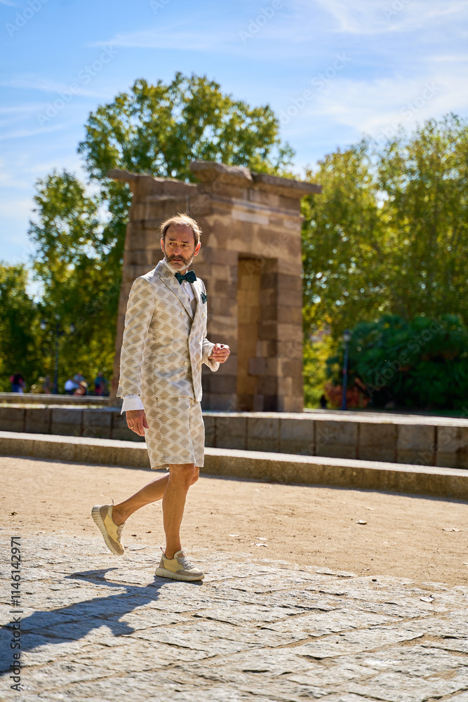 Man in patterned suit and shorts walking near an ancient structure outdoors Man in patterned suit and shorts walking near an ancient structure outdoors