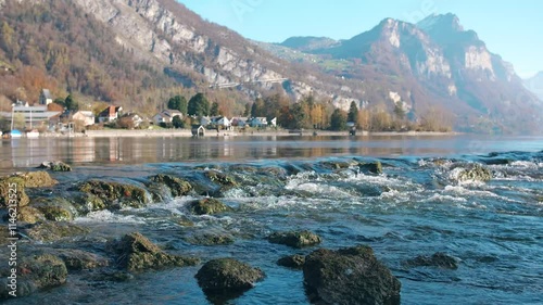 Clear waters of Walensee flowing over rocks with mountains and villages in the distance photo