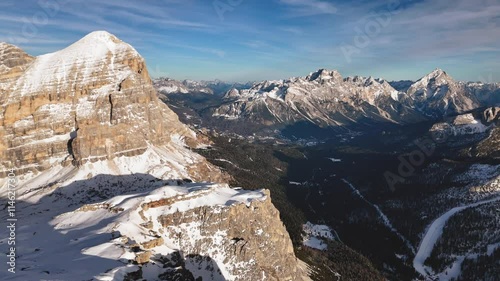 Breathtaking aerial view of a snow-covered mountain range under a clear blue sky with white clouds, enhancing the tranquility and serenity of the landscape. View from Rifugio Lagazuoi in Dolomites