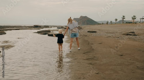 Travel mother and son walking at sand sea beach together holding hands enjoy summer vacation slowmo