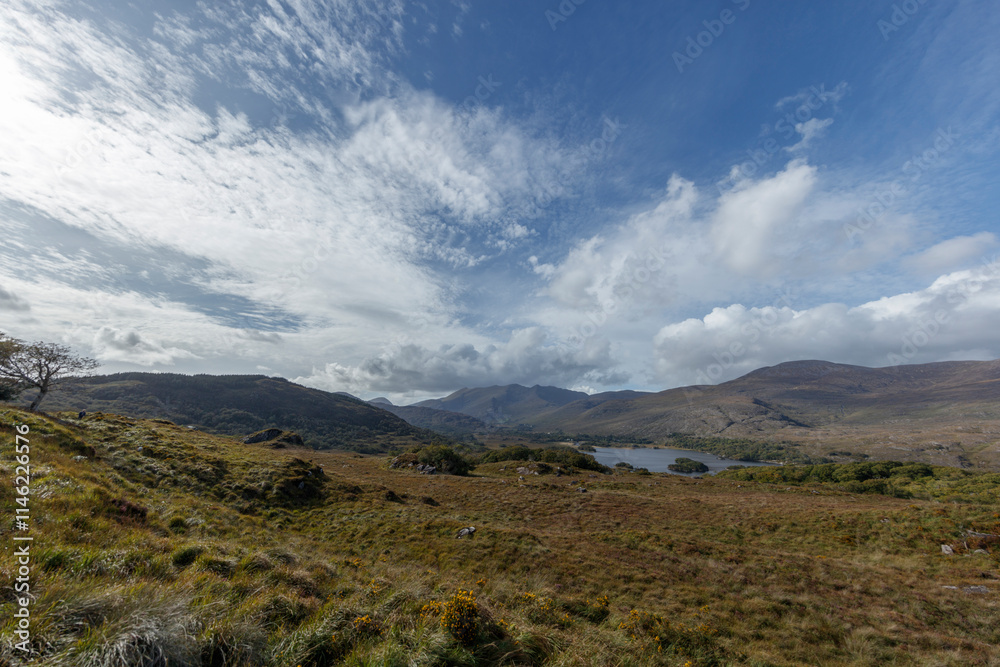 Panoramic view of Irish countryside. Rolling hills, lake, and a partly cloudy sky. Scenic landscape. Panoramic view of Irish countryside. Rolling hills, lake, and a partly cloudy sky. Scenic landscape.