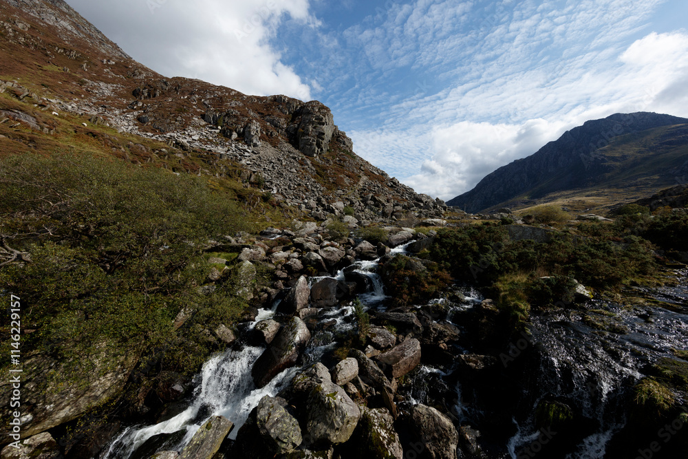 Mountainous landscape with a cascading stream. Rocky terrain, vegetation, and a clear blue sky are prominent. Mountainous landscape with a cascading stream. Rocky terrain, vegetation, and a clear blue sky are prominent.
