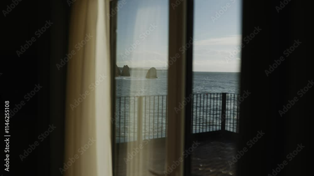 A view of the ocean from a balcony with a white curtain. The curtain is partially open, allowing a glimpse of the water. The scene is serene and peaceful