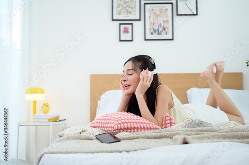 Young Asian woman wearing headphones enjoying music in bedroom at home photo