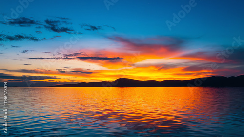 Vibrant sunset over calm lake reflects colorful sky and mountains in distance