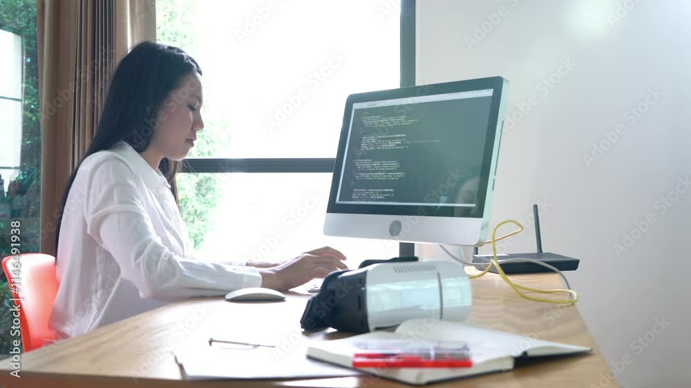 A woman is sitting at a desk with a computer monitor in front of her. She is typing on the keyboard and she is focused on her work A woman is sitting at a desk with a computer monitor in front of her. She is typing on the keyboard and she is focused on her work
