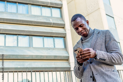 Portrait of an elegant and handsome black businessman using a smartphone in front of a m odern building in a city