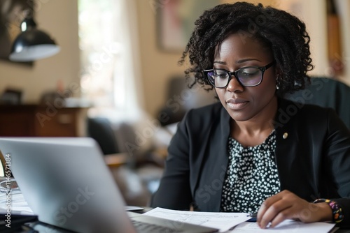 Professional woman working on financial documents at home office, focused on computer tasks and analyzing paperwork with dedication and precision