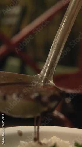 Closeup vertical slow motion footage of pouring feijoada on a plate of rice and steamed spinach
