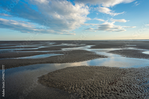 Sand at low tide with pools of water and ripples.