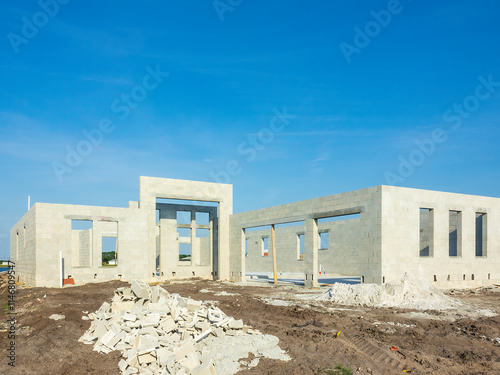 Concrete shell of a single-family house under construction, with piles of castoffs (left) and mortar mix (right) in front, in a suburban residential development on a sunny day in southwest Florida