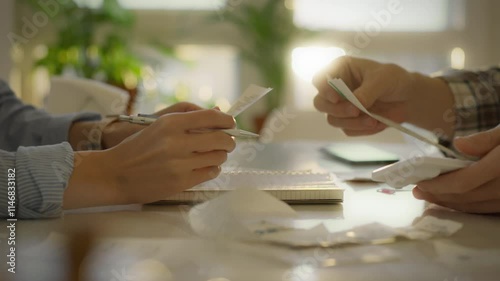 Two individuals are engaged in budget planning, sorting through receipts and using a calculator on a desk. The sunlight streams in, creating a productive environment for financial organization