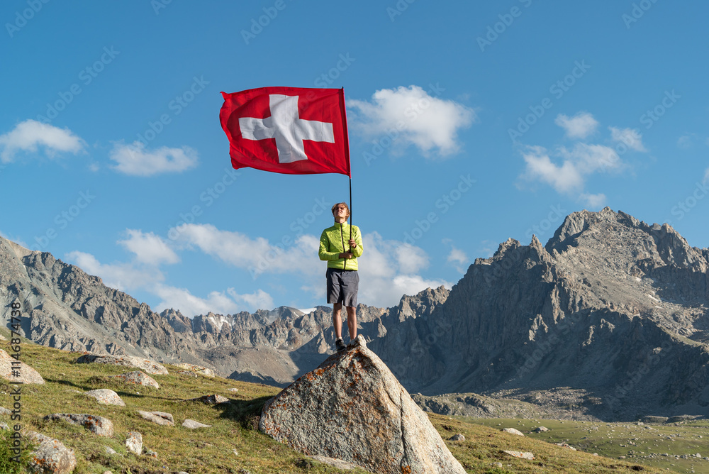 Obraz premium Young Man Holding Switzerland Flag Against mountain range. The tourist reached the summit.