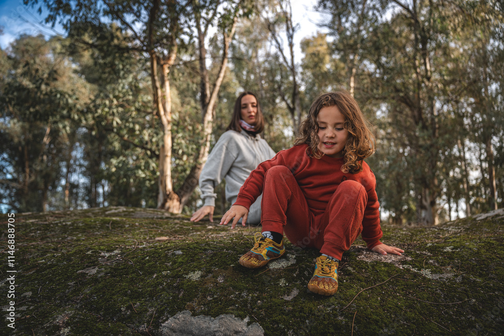 Fototapeta premium A young girl is sitting on a rock in a forest with her mother