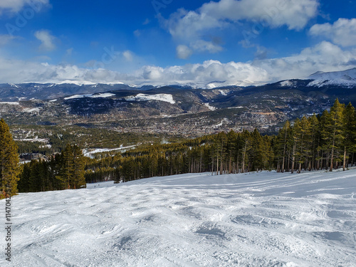 Ski resort run in the rocky mountains. Blue sky, wispy clouds. Powder snow. Trees covered in snow. Rocky mountain peaks background skyline.