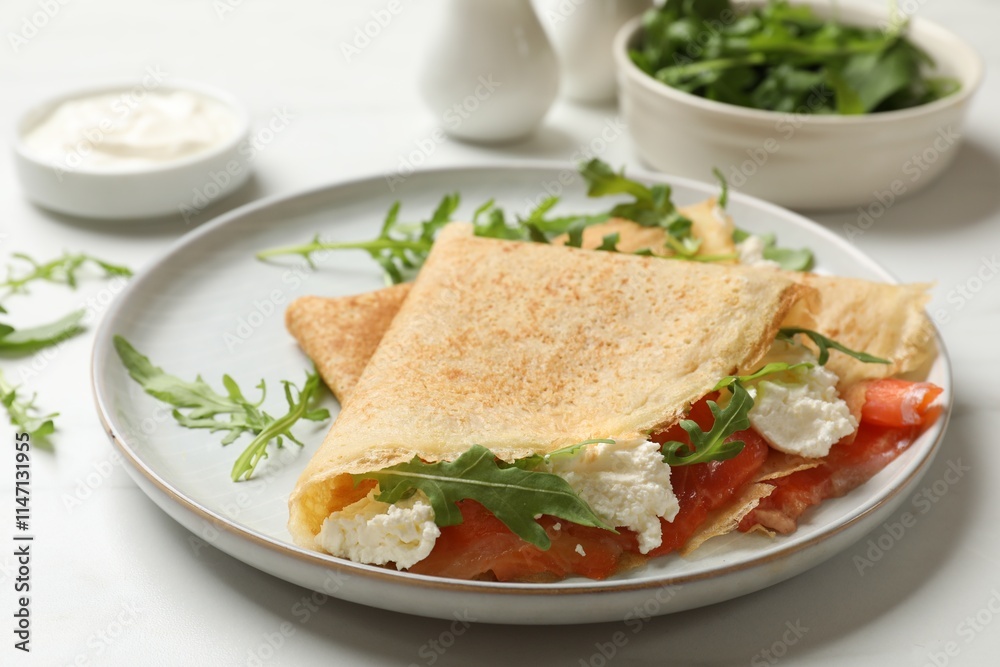 Delicious crepes with salmon, cream cheese and arugula on white table, closeup Delicious crepes with salmon, cream cheese and arugula on white table, closeup
