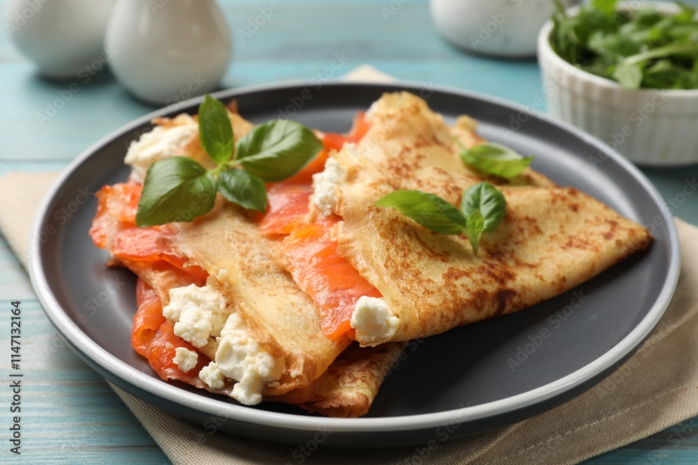 Delicious crepes with salmon, cream cheese and basil on light blue wooden table, closeup Delicious crepes with salmon, cream cheese and basil on light blue wooden table, closeup