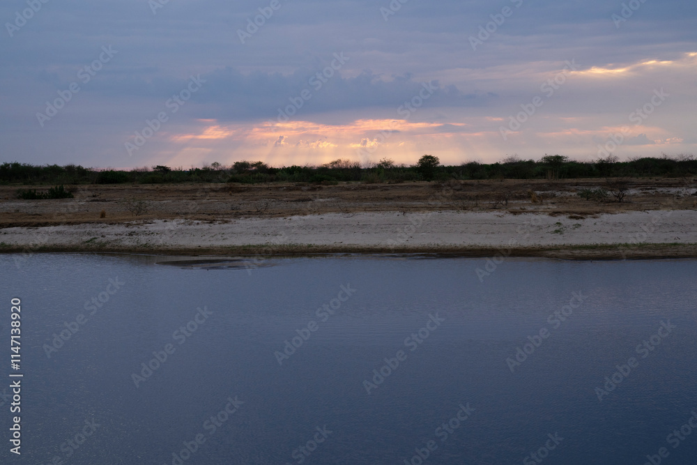 Magical view of the river and shore under a sunset sky with beautiful clouds. Enchanting reflection of the dusk colors in the water surface Magical view of the river and shore under a sunset sky with beautiful clouds. Enchanting reflection of the dusk colors in the water surface