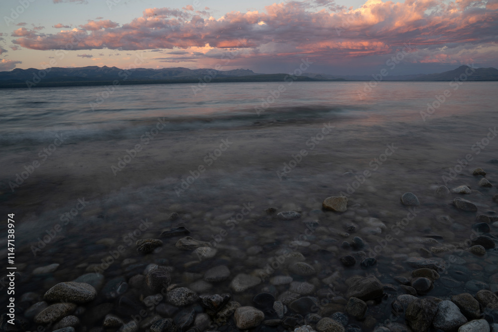 Obraz premium Long exposure shot of Nahuel Huapi lake at sunset. Beautiful blurred water effect, the rocky shore and dusk colors