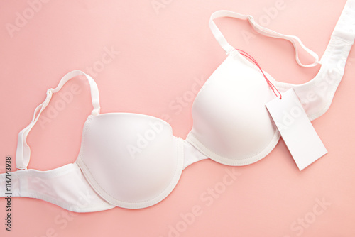White women's bra with white paper label on pink background