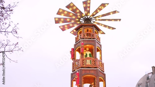 A beautifully illuminated wooden Christmas pyramid tower decorates the Paris Christmas market, adding warmth and tradition to the festive scene.  photo