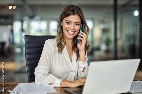 Happy smiling mature middle aged business woman, 40s professional lady executive manager talking on the phone making business call on cellphone at work in office using laptop computer.