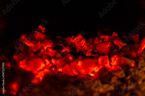 A close-up shot of glowing red hot coals in a fireplace. The fire has died down, leaving behind embers that still give off a warm glow.