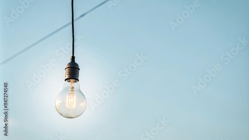 A single light bulb hangs from a wire against a clear blue sky, illuminating a sense of simple beauty and hope.