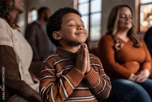 Little boy with closed eyes and clasped hands praying during a religious service inside a church