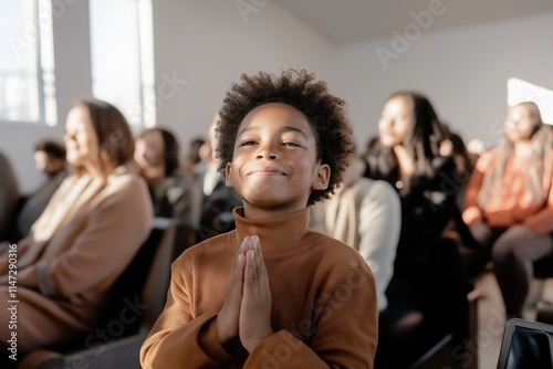 Hopeful african american boy with closed eyes and clasped hands praying in church during sunday service with congregation in background