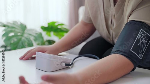 Woman measuring blood pressure with portable blood pressure monitor sitting on sofa in living room at home. Healthcare and medical concept.