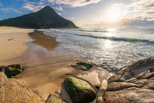 A bright sunrise over a rocky coastline and large mountain photo