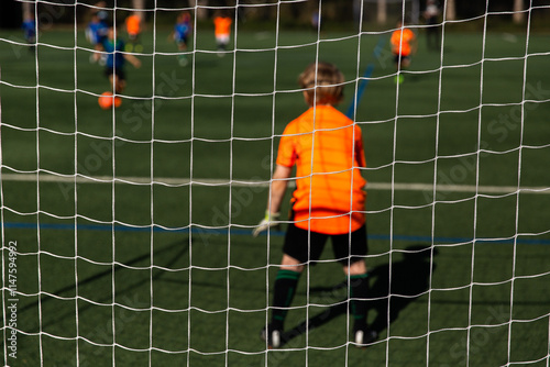 kids soccer game with a child in orange playing goal keeper on a sunny field photo