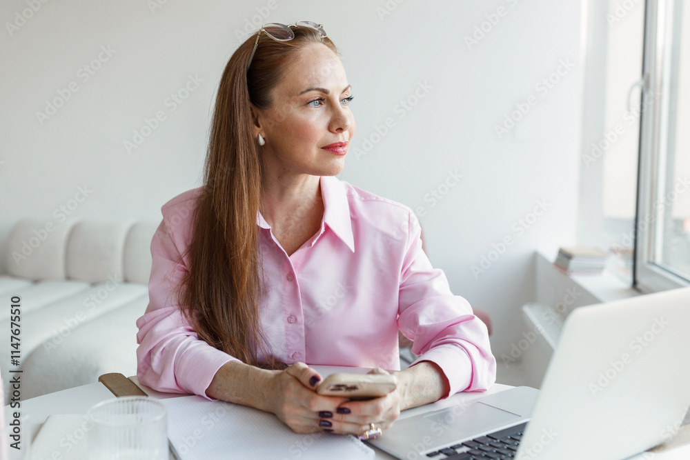 Portrait of intelligent businesswoman thinking of content of her message sending to her partners or clients to meet their requirements, sitting at desk with laptop on and looking through window Portrait of intelligent businesswoman thinking of content of her message sending to her partners or clients to meet their requirements, sitting at desk with laptop on and looking through window