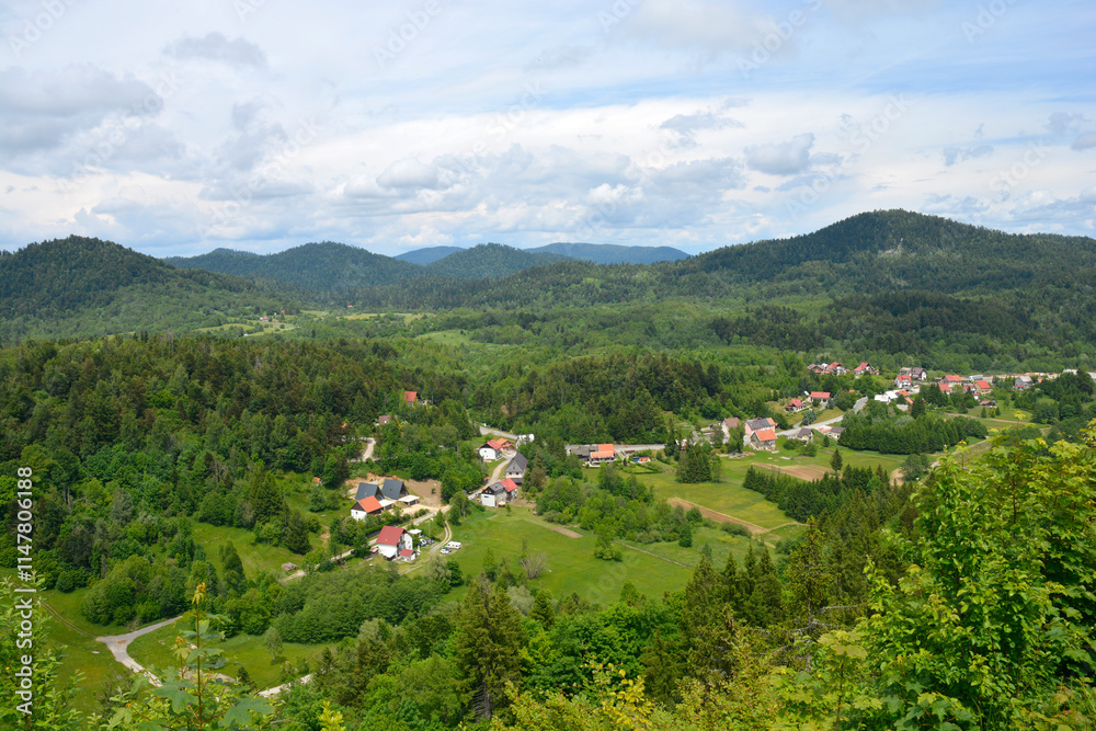 Obraz premium A view towards the municipality of Lokve as seen from a lookout point on the road above Lokve Lake (Lokvarsko jezero) in Croatia, featuring lush forests and picturesque village scenery