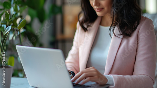 Woman in a stylish blazer typing emails on her laptop, modern and organized workstation, close up