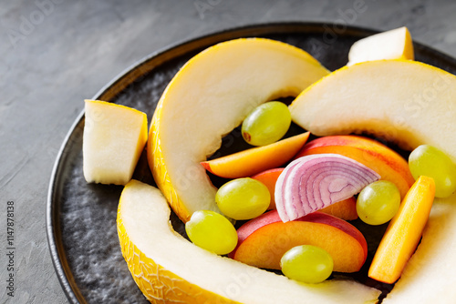 Fruit Salad on Black Plate, Melon Slices, Grapes, Peach and Red Onion, Close-Up