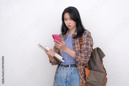 Asian female student carrying a backpack, reading messages from her smartphone photo