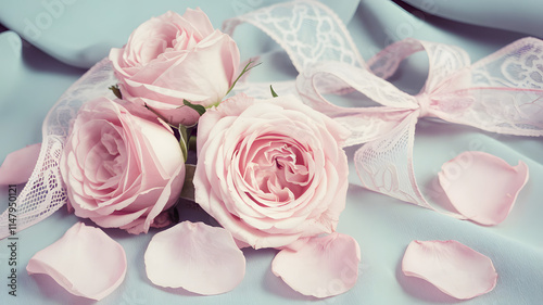 Delicate pink roses with lace ribbon and petals on a soft blue background, perfect for romantic occasions