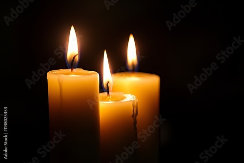 Three candles are lit and are burning brightly. The candles are arranged in a row and are lit up in a dark room. Scene is warm and cozy, as the candles provide a soft