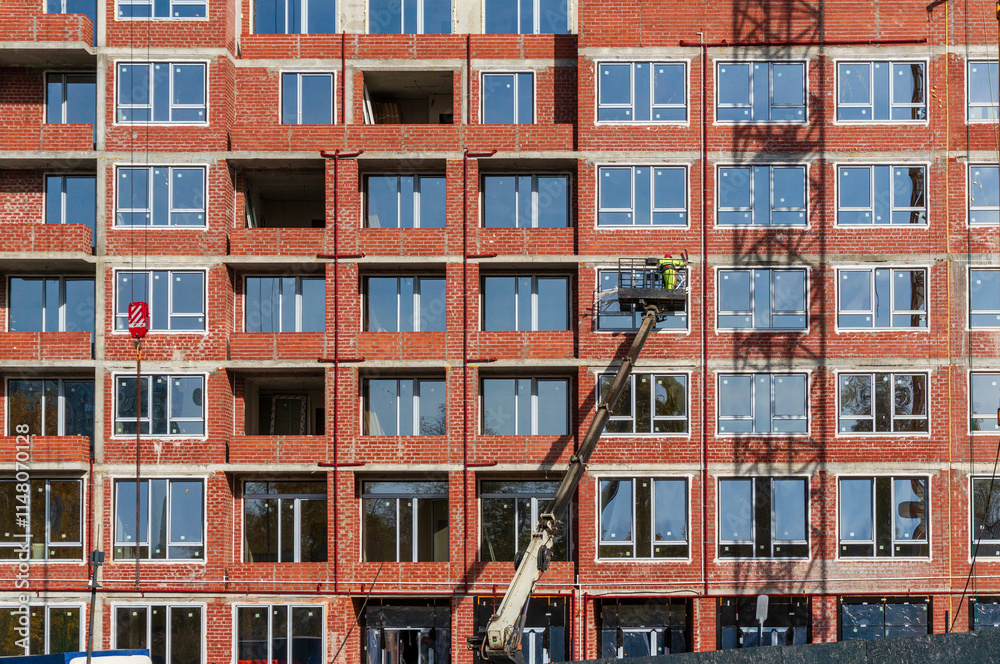 Naklejka premium Installation of double-glazed windows in a new multi-story residential brick building using a facade lift