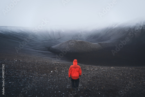 A male hiker in red jackets standing at the edge of the Hverfjall volcano, admiring the black tuff ring in snowy and misty weather photo