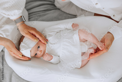 Billede på lærred A baby is laying on a white blanket with a white dress on