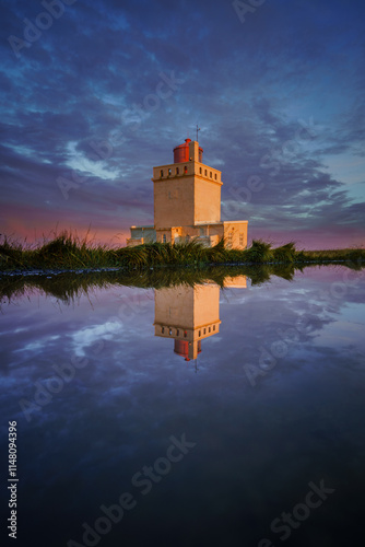 Iconic Dyrhólaeyjarviti lighthouse beautifully reflected in still water during a dramatic Icelandic sunset photo