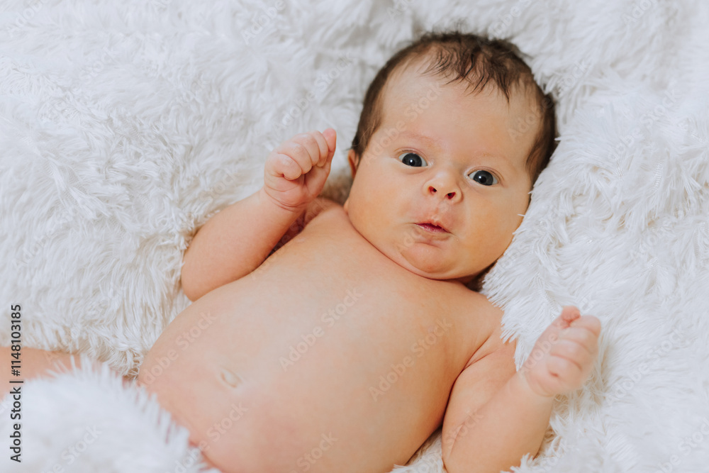 A baby is laying on a white blanket with its eyes wide open. The baby's face is bare, and it is looking at the camera. Concept of innocence and curiosity A baby is laying on a white blanket with its eyes wide open. The baby's face is bare, and it is looking at the camera. Concept of innocence and curiosity