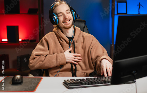 Happy positive gamer playing computer games at night at home, genuinely laughing holding his stomach. Gaming and E-sports training photo