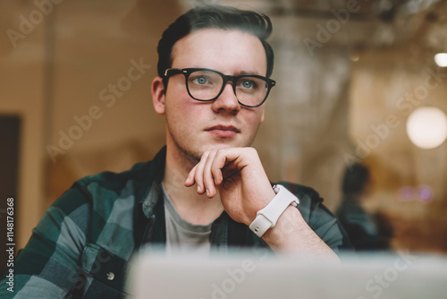 Serious male freelancer in spectacles pondering during working process on laptop computer in cafe interior, contemplative hipster guy thinking about solutions sitting near netbook studying online