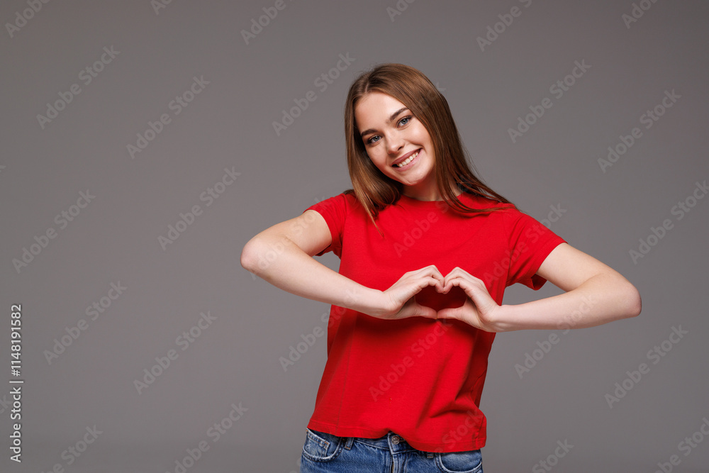Smiling pretty woman showing heart gesture with hands while standing isolated over gray background Smiling pretty woman showing heart gesture with hands while standing isolated over gray background