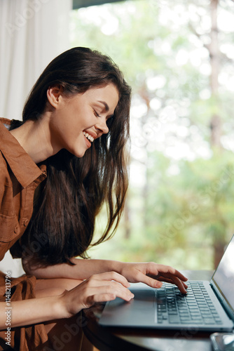 Cheerful young woman working on laptop with a beautiful nature backdrop, wearing a casual brown shirt, reflecting a positive and productive mood in a serene environment photo