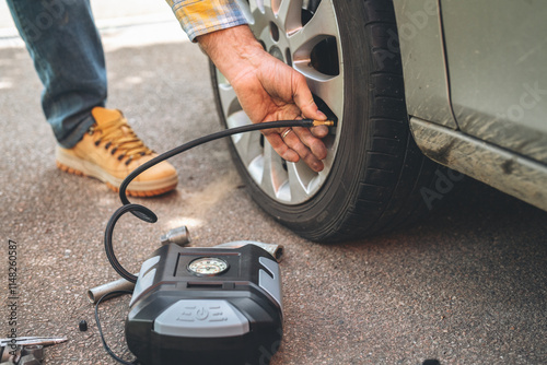 Man using a portable air pump to inflate car tire on a sunny day in a parking area